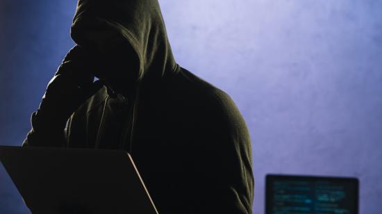 Imagen referencial de un ciberdelincuente frente al computador y con teléfono a mano, 6 de junio de 2025.