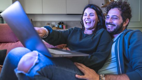 Pareja observa contenido en una laptop mientras comparte un momento en casa.