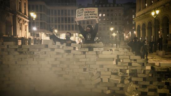 Un manifestante detrás de una barricada sostiene una pancarta que dice: "Su poder se mantiene en pie mientras nuestra rabia se mantiene sentada", en medio de protestas por "el alto costo de la vida" en Lyon, Francia, el 17 de octubre de 2026.