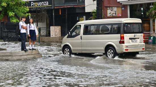 Estudiantes permanecen en la acera de una calle inundada en el barrio de Urdesa, al norte de Guayaquil, el 26 de octubre de 2026 tras una fuerete lluvia y tormenta eléctrica.