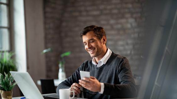 Empresario feliz trabajando con una computadora y un smartphone.