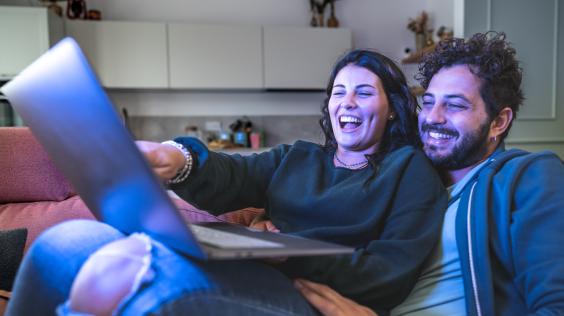 Pareja observa contenido en una laptop mientras comparte un momento en casa.