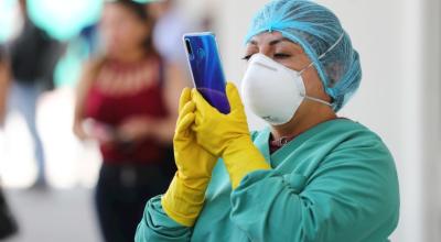 Una doctora con traje de protección observa su teléfono mientras trabajadores del municipio de Quito desinfectan unidades de transporte, 13 de marzo de 2020.