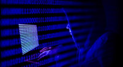 Una persona vestida como un pirata informático con un código binario que se muestra en la pantalla de una computadora portátil.