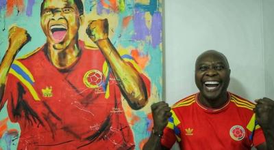 Freddy Rincón sonríe posando la camiseta de la selección colombiana junto a cuadro en donde aparece su imagen.