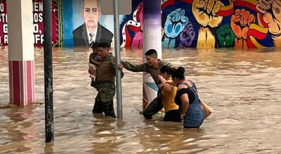 Personal del Ejército ayuda a varias personas a cruzar por una calle inundada en Chone, el 8 de marzo de 2023. 