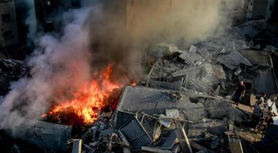 Algunos palestinos buscan entre los escombros de un edificio arrasado mientras el humo y el fuego se elevan tras un ataque israelí, en la ciudad de Gaza el 26 de octubre de 2023, en medio de la guerra entre Israel y el grupo Hamás.