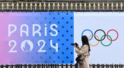 Transeúnte toma una fotografía de una pancarta de los próximos Juegos Olímpicos de París 2024 frente a la Asamblea Nacional en París, el 5 de mayo de 2024.