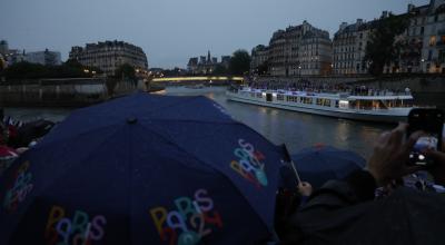 Miembros del público se protegen de la lluvia con paraguas mientras observan el desfile de las delegaciones por el río Sena.