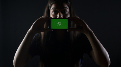 Fotografía ilustrativa de una mujer que desde la oscuridad sostiene un celular con el logo de WhatsApp en su pantalla.